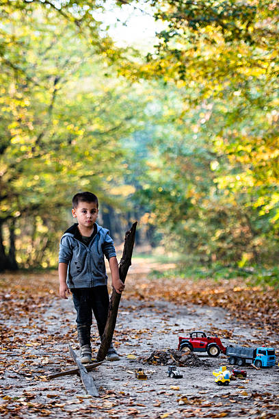 istock Young boy playing with stick and toy trucks in autumn forest 2232189113