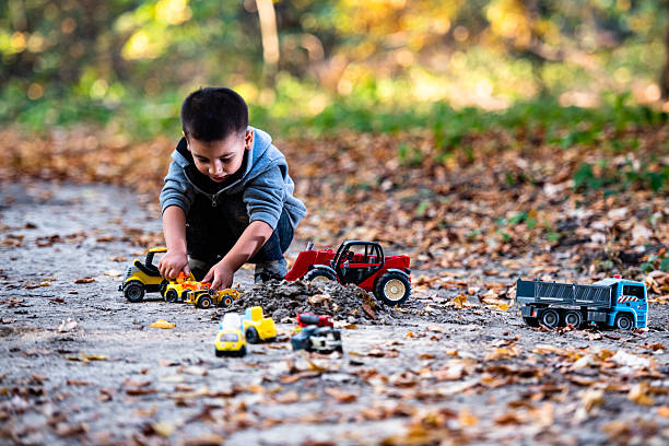 Preschooler joyfully playing with colorful toy trucks and construction vehicles amidst vibrant autumn leaves in a serene forest setting