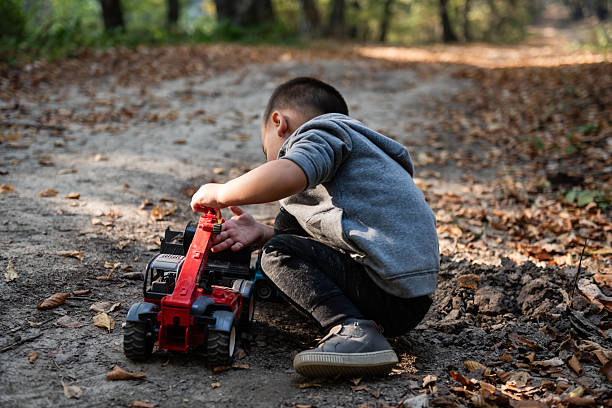 Young child playing with a toy crane truck in a forest path covered with dry leaves during a sunny autumn day