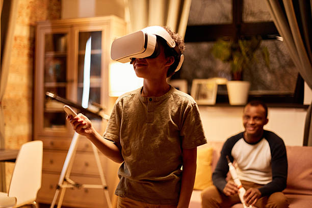 istock Father sitting on couch holding toy rocket looking at son using VR headset 2232192318