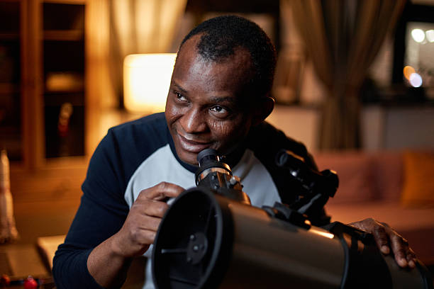 Portrait of mature Black man learning astronomy enjoying watching stars and planets using telescope at home