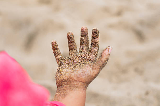 Child showing their hand covered in sand on a sunny beach, enjoying a summer day playing outdoors. Lifestyle concept