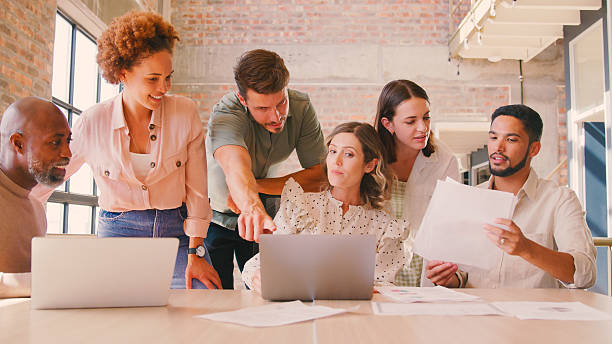 istock Multi-Cultural Business Team Meeting Around Laptop Discussing Documents In Busy Office 2232197741