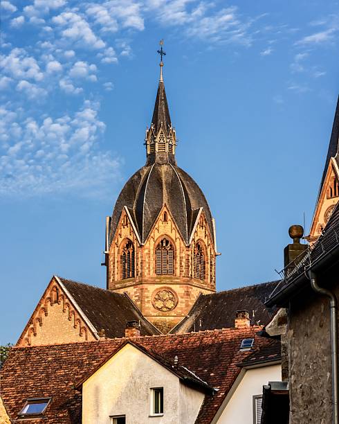 A stunning church steeple rises above traditional European rooftops under a bright blue sky in a quaint village setting.