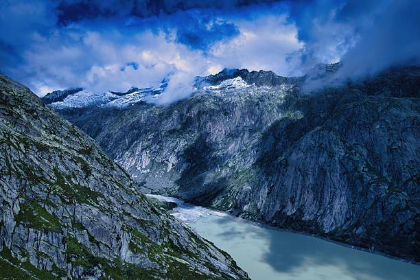 A breathtaking view of a mountainous landscape with dramatic clouds and a serene lake below, showcasing the beauty of nature.