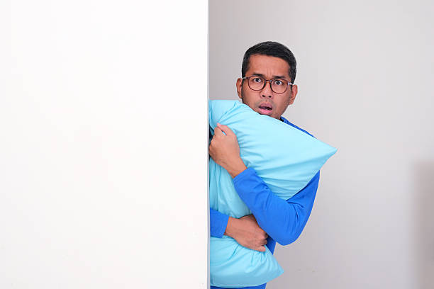istock Adult Asian man peeking behind wall hugging a pillow with scared expression 2232199745