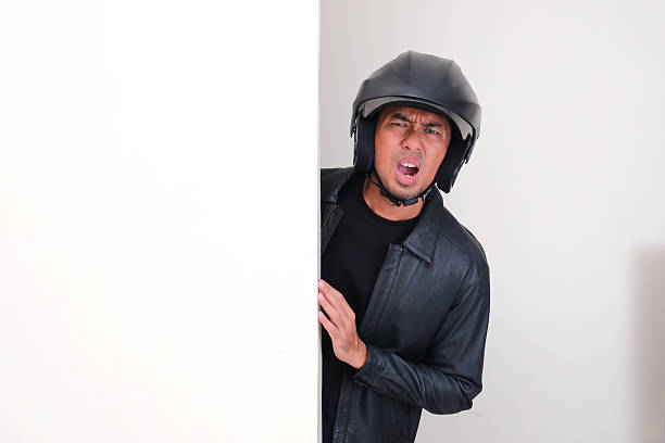 istock Motorcycle rider wearing helmet peeking from behind wall showing disappointed expression 2232200562