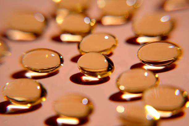 Softgels or capsules creating reflections on a pink background, representing health, wellness, and pharmaceutical products