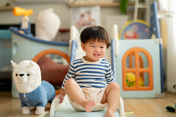Happy Asian toddler boy laughs joyfully while playing on plastic slide toy, demonstrating gross motor development and emotional regulation through active play exploration and sensorimotor learning experiences