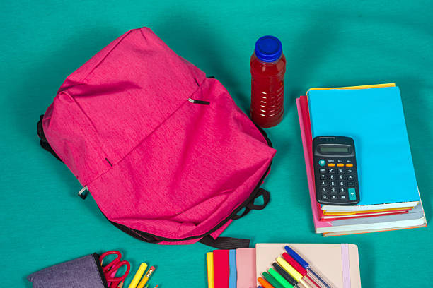 Arranging school supplies like a pink backpack, books, and colorful stationery on a teal background, creating a vibrant scene for student preparation