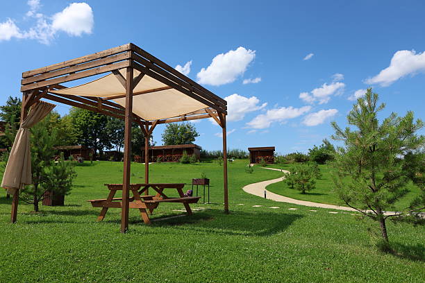 Summer outdoor resort with hammocks, wooden gazebos, volleyball court, garden sink, and lifebuoy near a lake. Captured in natural daylight with a wide-angle lens.