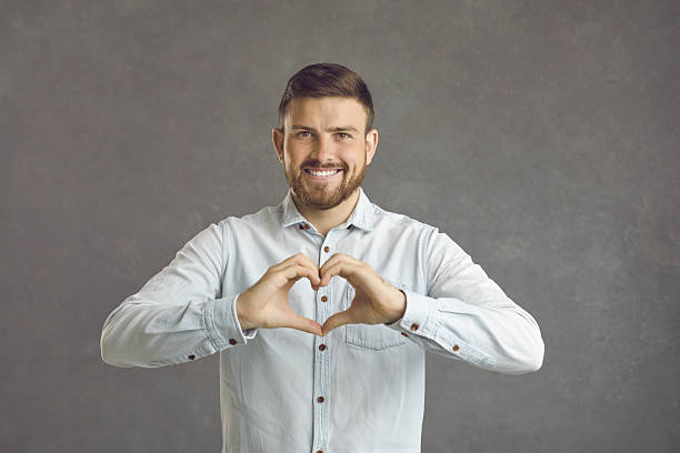 istock Handsome caucasian young man expresses a gesture of love while standing on a gray background. 2232230609