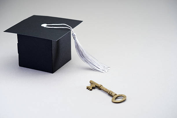 small mortarboard and antique key against white background.