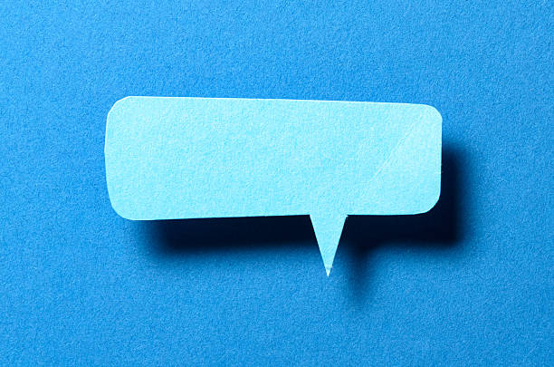 Blank cut out paper speech bubble with shadow and copy space for text on blue background, close-up flat lay top view conceptual backdrop