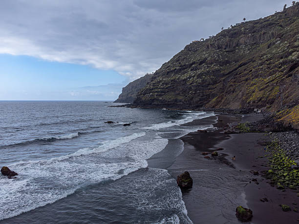 istock Drone view above a black sand beach from Atlantic Ocean with foamy white waves breaking on it. El Ancon Beach in Tenerife, Spain 2232246409