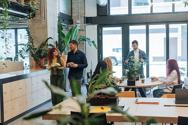 Diverse business group of happy coworkers and male leader talking in modern workspace, meeting in co-working, discussing teamwork, project strategy, laughing, having fun together