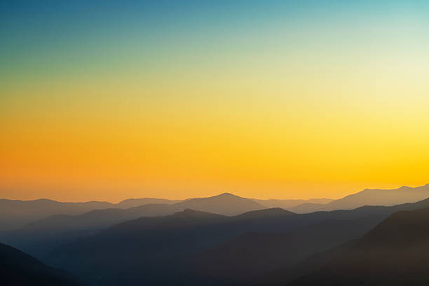 Sunset scene featuring rolling hills in silhouette against a color gradient sky of orange and blue tones, evoking tranquility and natural beauty.