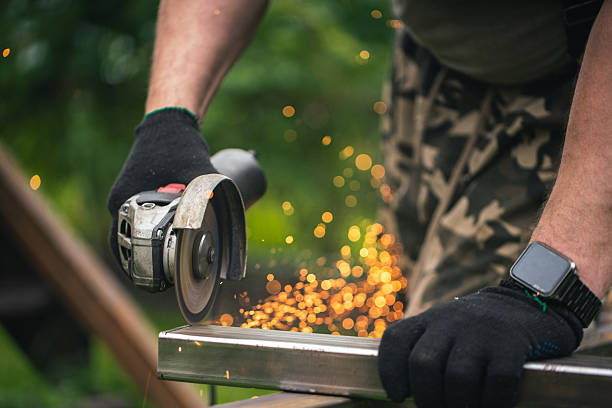Metalworking process outdoors featuring a worker using an angle grinder emitting bright sparks, displaying precision craftsmanship and hardworking dedication in a vibrant natural setting.