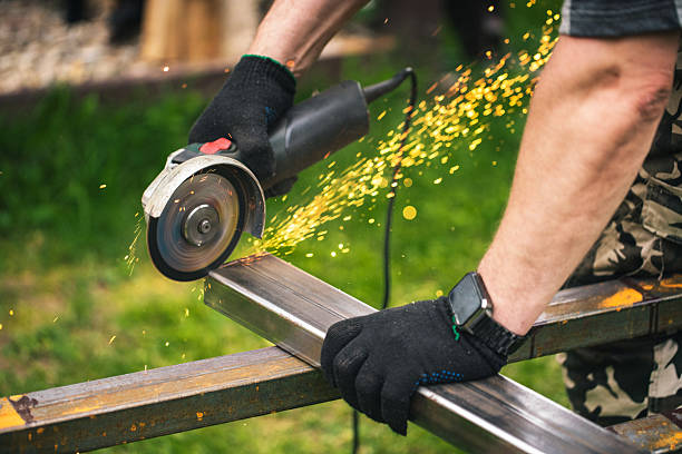 A close-up of a person using an angle grinder to cut a metal bar outdoors. Sparks are flying, indicating the intensity of the task, highlighting craftsmanship and industrial themes.