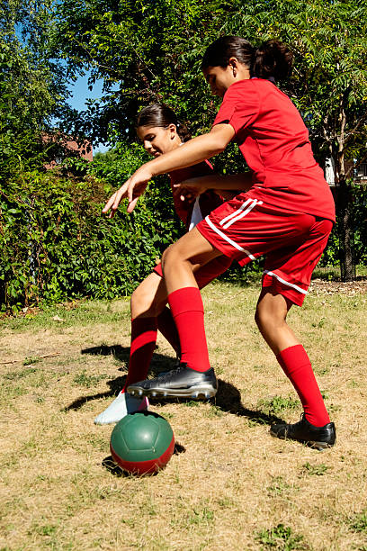 Sisters playing soccer in city backyard. They are from middle eastern descent and are wearing red traditional soccer clothing. Vertical full length outdoor shot with copy space. This was taken in Montreal, Quebec, Canada.