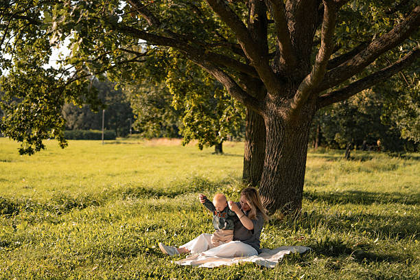 istock A mother and her baby are sitting on a blanket under a large, thick tree. 2232262638