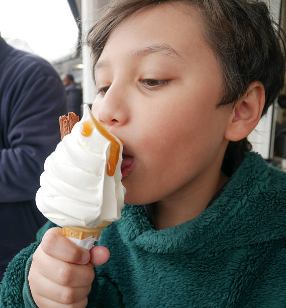 Portrait of Black boy smiling and licking ice cream cone outdoors, showing joyful facial expression and direct eye contact with camera, casual setting in background