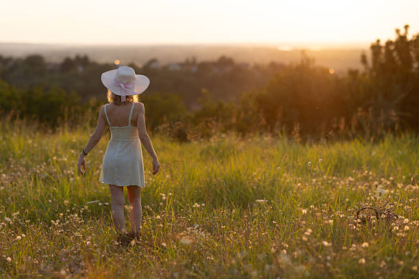 A serene moment as a woman explores a picturesque meadow under the golden hues of sunset.