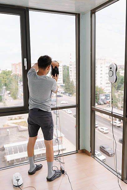 istock Rear view of housekeeper male using advanced robotic device for cleaning large window in modern high-rise, representing innovative window maintenance technology. 2232275851