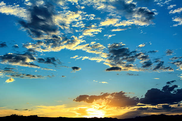 Golden Sun Setting Behind Spring Mountains over the Mojave Desert, Las Vegas, Nevada Illuminating a Bright Blue Sky and Dramatic Clouds