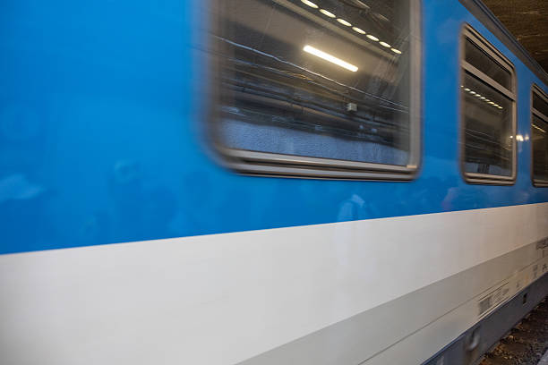 A close-up photograph captures the side of a blue-and-white train speeding past Monterosso station in Cinque Terre, Italy. The windows and stripes appear blurred due to the train’s motion, conveying a sense of dynamic travel, energy, and the pace of modern transportation along the scenic Ligurian coast.