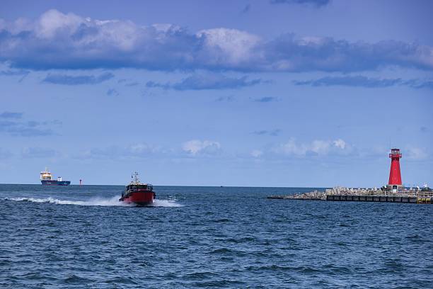 istock Bright red boat navigates through calm waters near coastal lighthouse under blue sky 2232307510