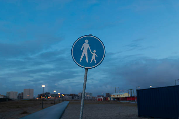 Blue pedestrian crossing sign with parent and child icons against blurred evening cityscape background