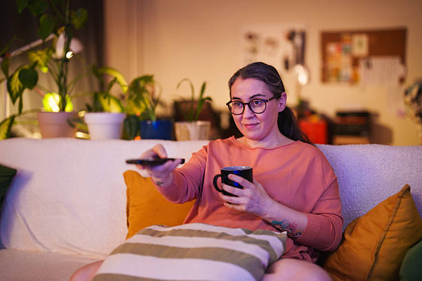 istock Woman sitting on sofa with remote control and cup of coffee 2232316294