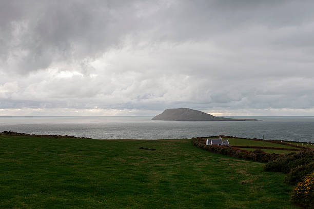 Green Welsh coastal fields with white cottage and island view under dramatic sky