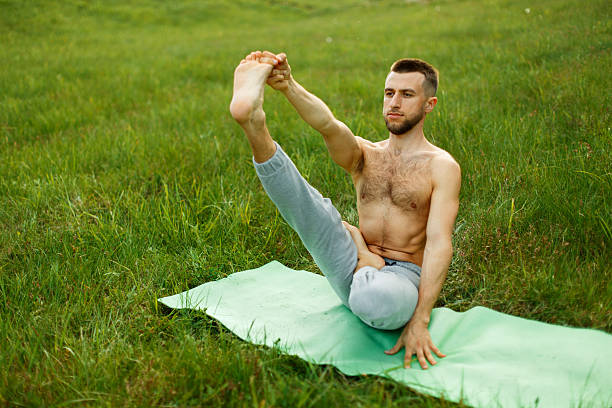 Young man doing the boat pose during yoga practice in the park
