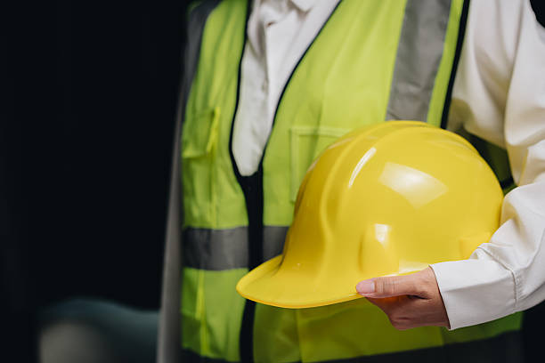istock Construction Worker Holding Yellow Hard Hat in Safety Vest with Reflective Stripes in Indoor Setting 2232324714
