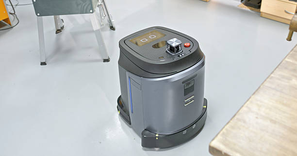 A modern grey robotic floor scrubber sits on a clean concrete surface in a workshop, designed for automated maintenance in technical or manufacturing environments.
