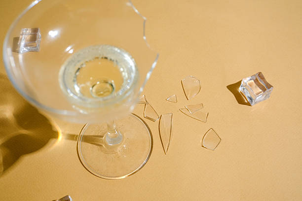 istock Broken glass with drink and ice cubes on sandy surface, sharp fragments scattered around 2232329746