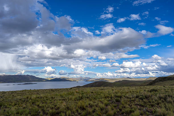 Lake Lagunillas in Peru is surrounded by rolling hills and grasslands, with dark storm clouds above and a distant rain shower falling over the mountains