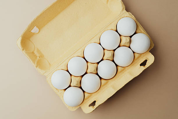 istock White eggs in yellow carton top view on beige background 2232330063