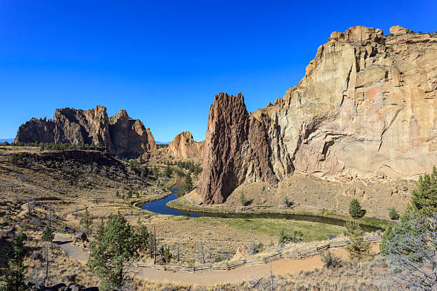 The Crooked River flowing past the Phoenix Buttress in Smith Rock State Park, Oregon, USA, surrounded by dramatic cliffs and desert scenery.