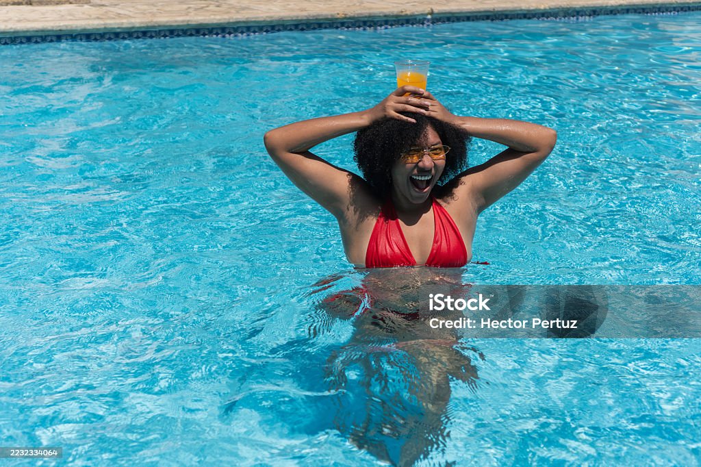 Mujer joven divirtiéndose en la piscina con jugo de naranja - Foto de stock de 20 a 29 años libre de derechos Mujer joven divirtiéndose en la piscina con jugo de naranja - Foto de stock de 20 a 29 años libre de derechos