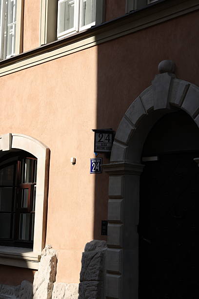 Sun-drenched architectural detail: a peach-toned building's facade, featuring arched stonework, a shadowed doorway, and a numbered plaque.