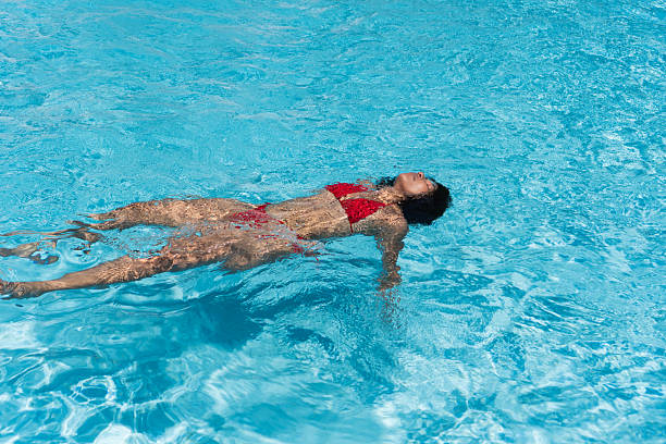 istock Young woman floating on back in swimming pool wearing red bikini 2232334533