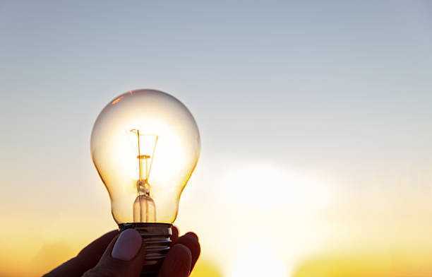 Light Bulb Held Against a Vibrant Sunset in a Clear Sky
