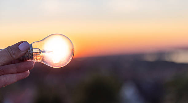 istock Hand Holding Light Bulb Against a Beautiful Sunset Horizon at Dusk 2232336209