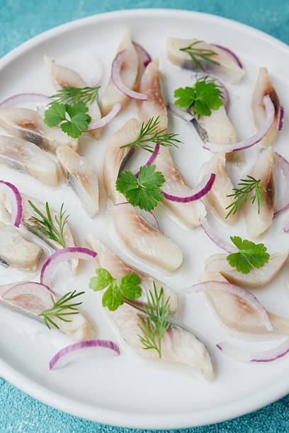 istock Marinated herring slices with red onion and herbs on white plate over blue background 2232337370