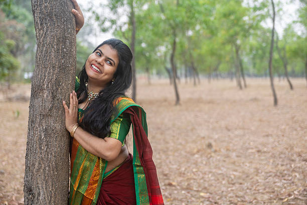 A pretty Indian woman in red saree and long hair posing smiling outdoors with tree