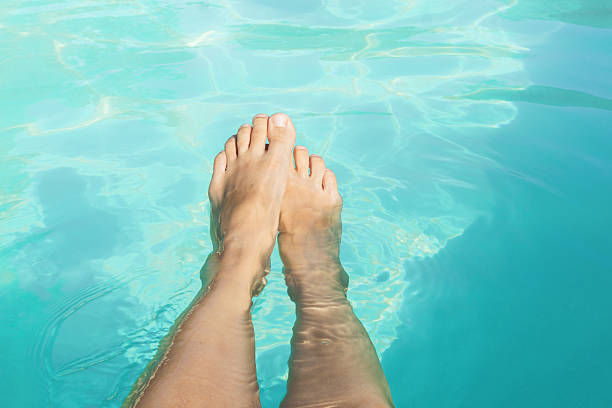 Legs are submerged in clear, blue pool water, reflecting sunlight on a warm summer day. Perfect moment for relaxation and soaking in the refreshing atmosphere of a retreat.