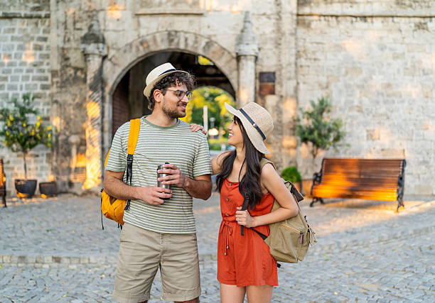 Young couple with backpacks walking and chatting in front of an ancient gate during their summer vacation